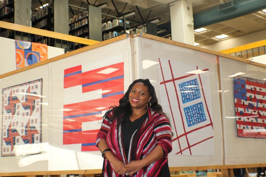 Dominique Dozier stands in front of colorful quilt display at Laney Library